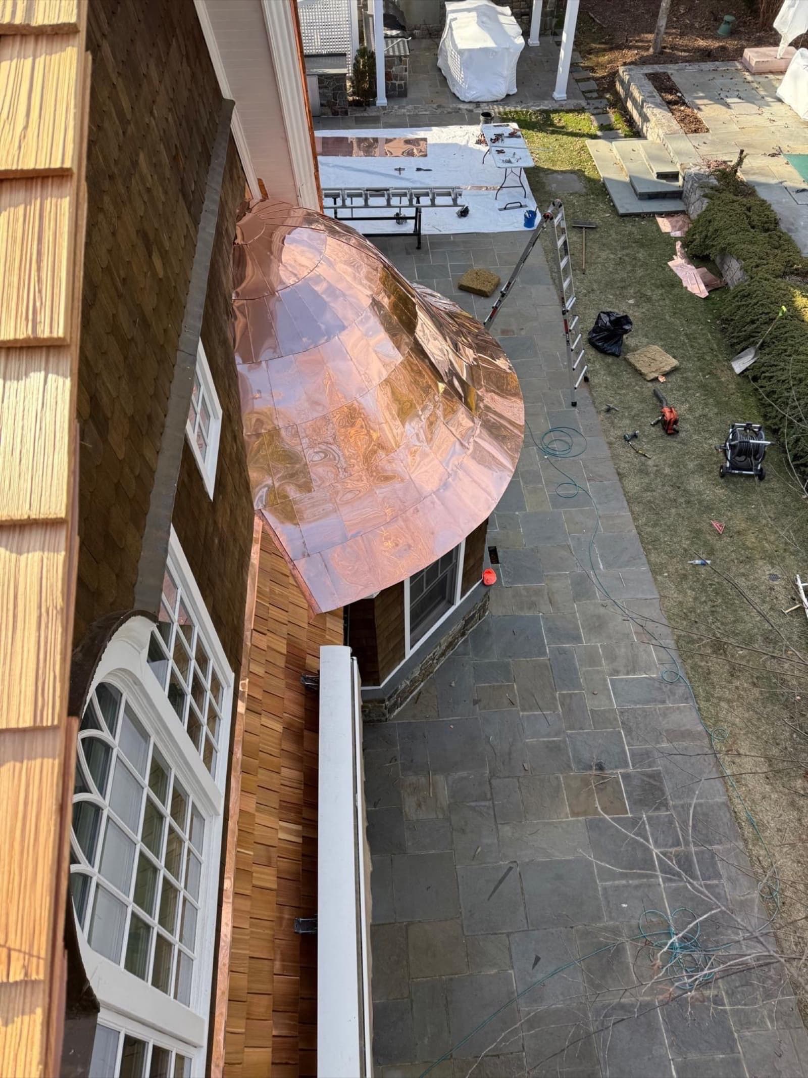 Curved copper bay-window roof on a cedar-shake luxury home — custom metal roofing detail by Zubar Roofing.