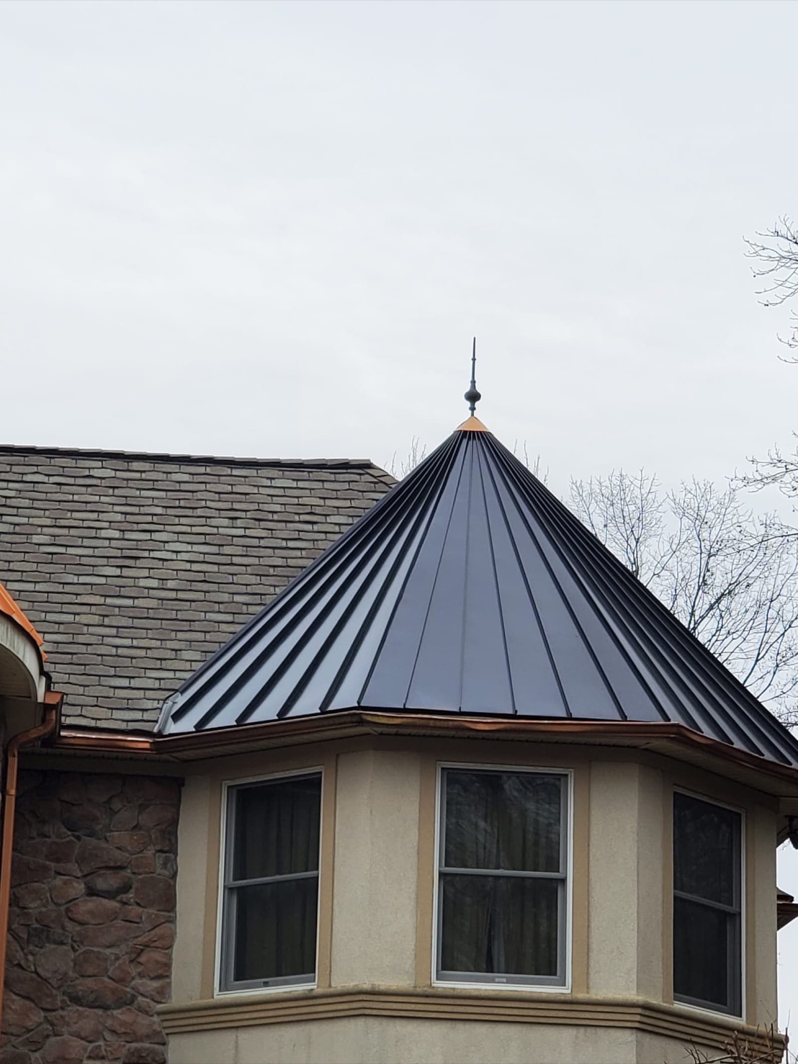 Black standing-seam metal roof installed on a stone-and-stucco turret in New Jersey by Zubar Roofing — concealed-fastener panels.