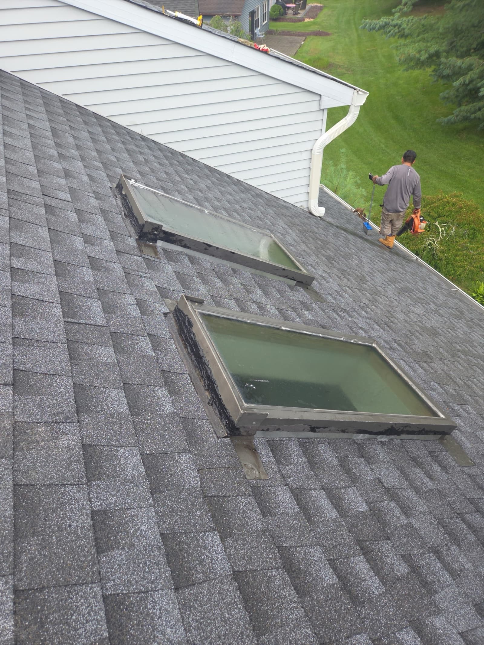 Roof maintenance and skylight reseal on a gray architectural shingle roof in New Jersey by a Zubar Roofing technician.