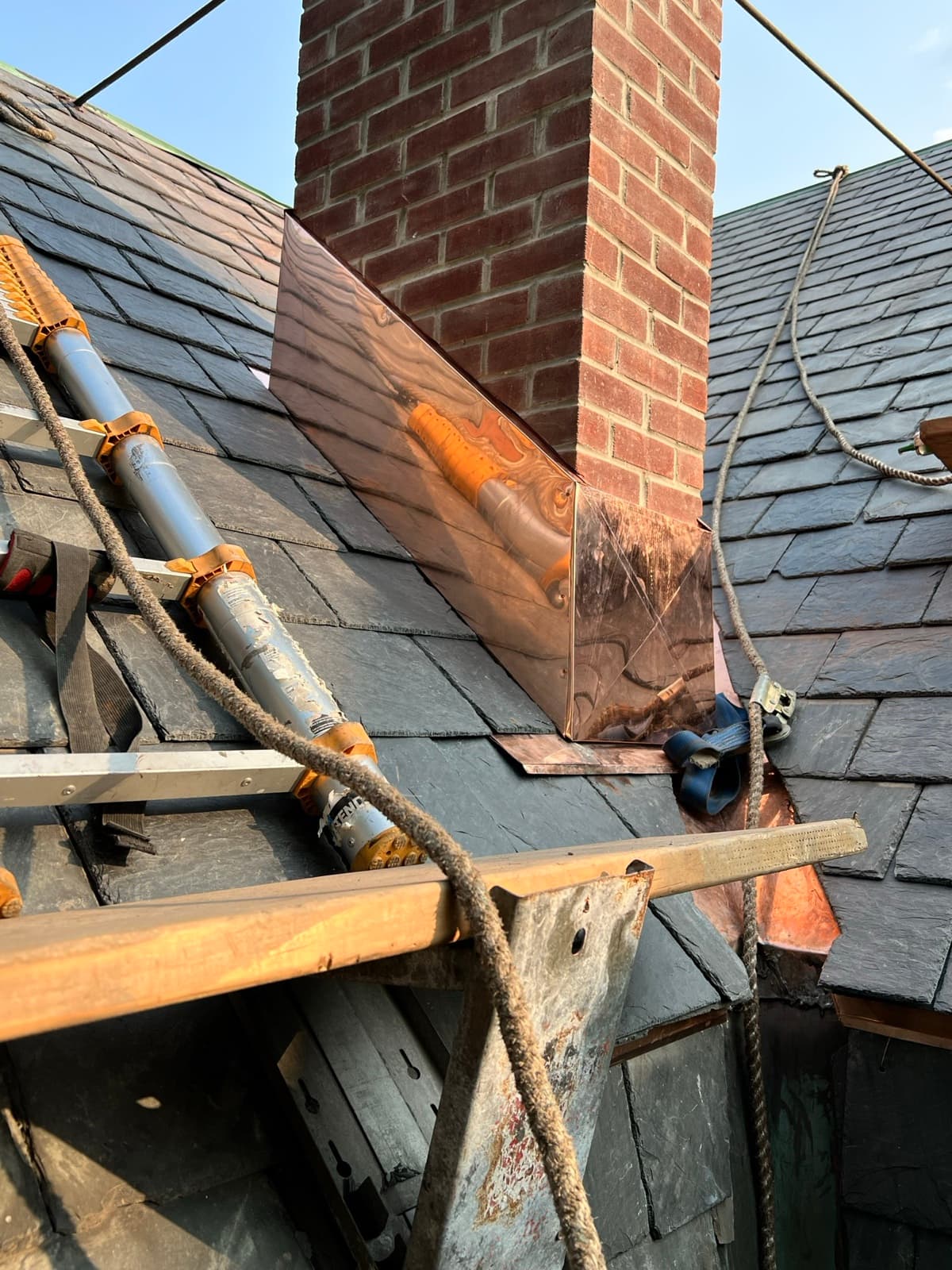 Roof repair on a slate roof in New Jersey — new copper step flashing installed around a brick chimney by Zubar Roofing.